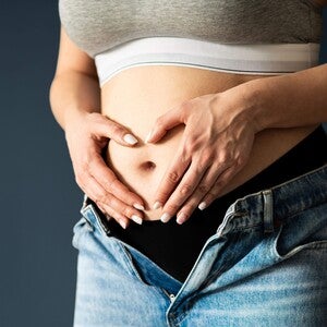 Abdomen de mujer embarazada en primer o segundo trimestre, manos en forma de corazón sobre el vientre.