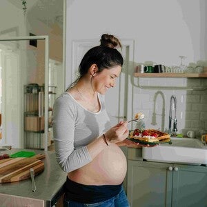Mujer embarazada sonriendo en la cocina comiendo antojo dulce