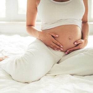 Mujer embarazada sentada en la cama sosteniendo su vientre.