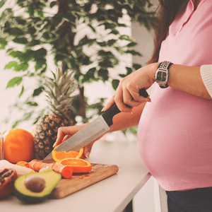 Pregnant woman slicing an orange by a kitchen counter full of fruit. Pregnant woman slicing an orange by a kitchen counter full of fruit.