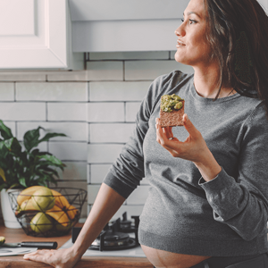 Dreamy looking pregnant woman, standin on her kitchen eating an avocado toast Dreamy looking pregnant woman, standin on her kitchen eating an avocado toast