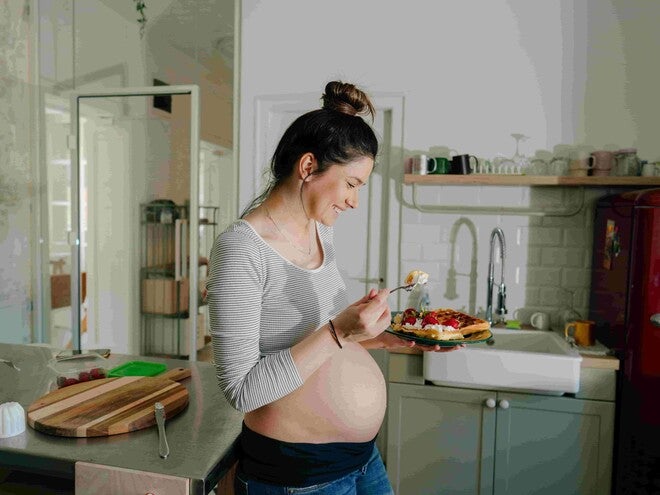 Mujer embarazada sonriendo en la cocina comiendo antojo dulce