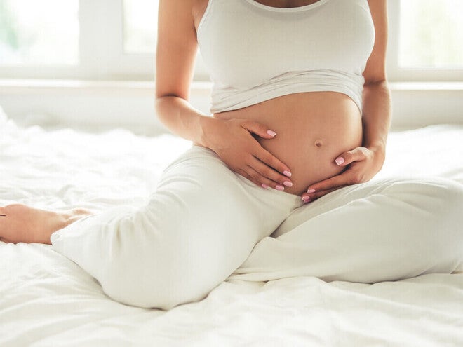 Mujer embarazada sentada en la cama sosteniendo su vientre.