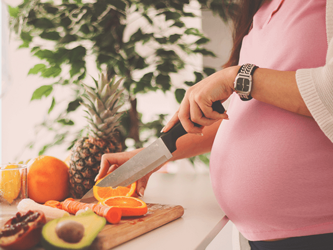 Pregnant woman slicing an orange by a kitchen counter full of fruit. Pregnant woman slicing an orange by a kitchen counter full of fruit.