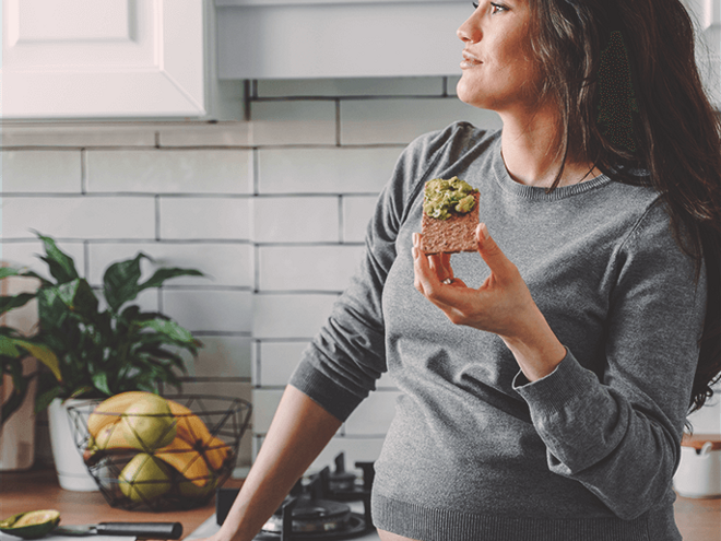 Dreamy looking pregnant woman, standin on her kitchen eating an avocado toast Dreamy looking pregnant woman, standin on her kitchen eating an avocado toast