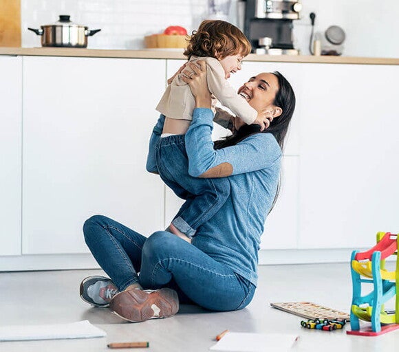 Tips de crianza positiva Madre jugando con su bebé en el suelo en una parte de la cocina